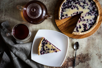 Delicious blueberry pie on a beautiful wooden plate, a Cup of hot tea, a teapot with tea and a piece of blueberry pie on a white plate