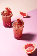 Fresh summer cocktail with pink grapefruit slices. Divided pink and beige bankground. Abstract conception.