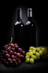 Obraz na płótnie Canvas Two bunches of grapes on a dark background with two bottles of wine. A studio photo.