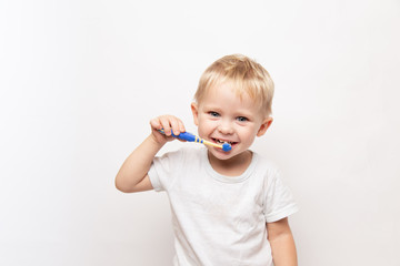 little cute caucasian blond blue-eyed boy in a white t-shirt brushes his teeth on a white background