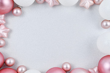 Seasonal Christmas background with white and pink tree baubles forming border around empty copy space with silver white glitter background