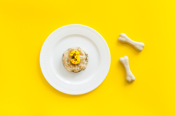Birthday party for puppy concept. Dog feed, candle in shape of number three, bones on yellow background top-down
