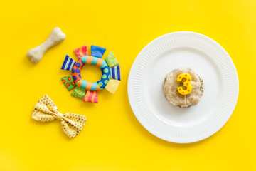 Birthday party for puppy concept. Dog feed, candle, bone, bow-tie on yellow background top-down