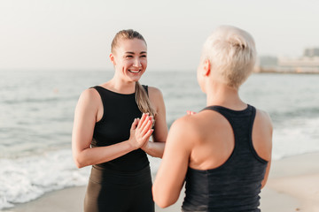 sporty woman smiling and laughing on the beach near ocean where she meditates together with mother