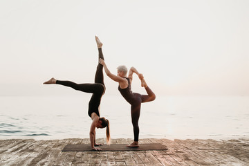 Fototapeta na wymiar woman exercising acro yoga on the beach near sea in the morning with mature female tutor