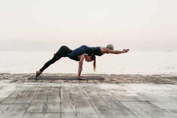 women practising acro yoga asana near sea on sunrise