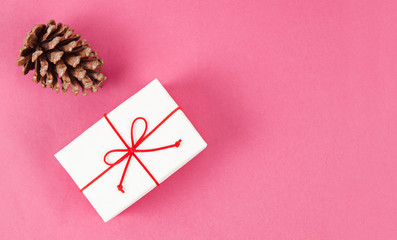 White gift box and pine cone on pink background.