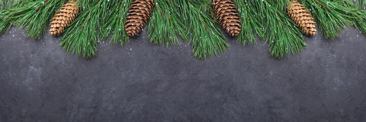 Christmas background with tree branches and cones on black stone background. Snowfall drawing...