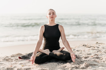concentrated woman meditating in yoga pose on the beach near ocean