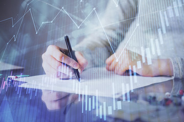 Hand taking notes in notepad. Forex chart holograms in front. Concept of research. Multi exposure