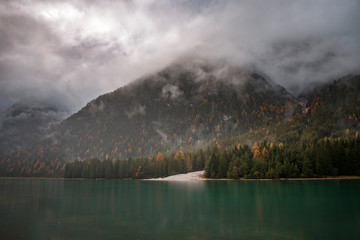 Turquoise colour lake South Tyrol, Italy , Alps. Reflection in water during rain (high ISO long exposure image) Dark green forest in background.