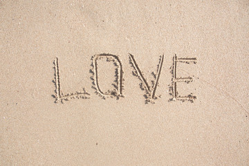 Word LOVE drawn on the sand of sandy beach.