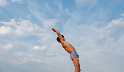 athletic teenager on the beach in swimming trunks against the sky