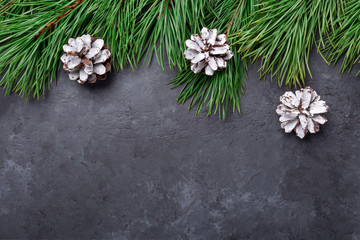 Christmas background with tree branches and cones on black stone background. Snowfall drawing...