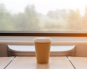 Disposable Cup of coffee is on the table in the train. Big window, sun light.
