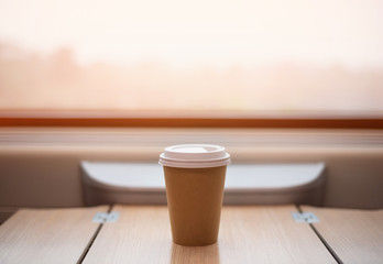 Disposable Cup of coffee is on the table in the train. Big window, sun light.