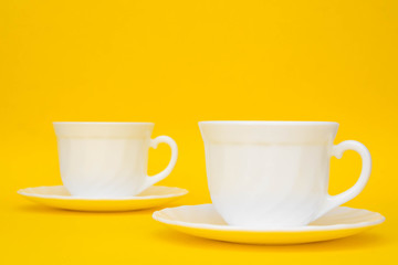 White ceramic cups with saucers on yellow background. White tableware crockery set. Space for text