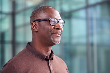 Head And Shoulders Shot Of Mature Businessman Standing In Lobby Of Busy Modern Office