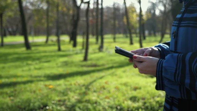 Woman`s hands holding a smartphone and surfing the net it in a park in slo-mo 