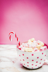 Pink white mug with marshmallows, sugar cane on a marble surface with pink background