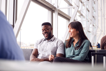 Business Couple Sitting By Window Waiting In Airport Departure Lounge