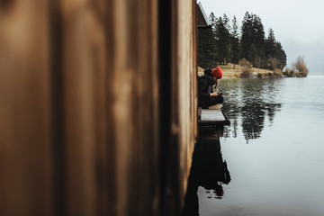 Boathouse at lake plansee in fall mood during fog and rain, female in red hat sitting on wooden deck