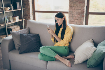 Obraz premium Profile side view photo of cheerful positive girl sit divan use her smartphone read social network news wear casual style clothing in room indoors