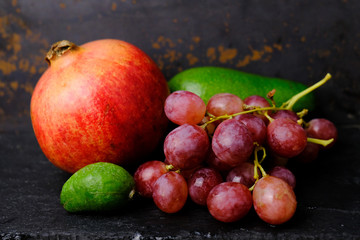 Fruit and berries background. Healthy food. Pomegranate, avocado, feijoa and bunch of grapes. Natural vitamin.