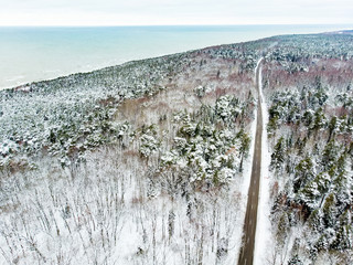 Beautiful aerial view of snow covered pine forests and a road winding among trees. Scenic winter landscape near Vilnius, Lithuania.