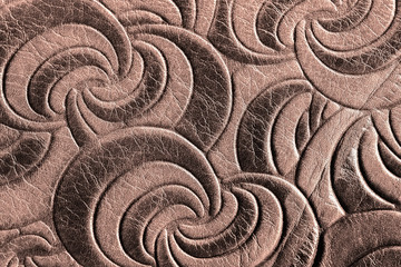 Texture of brown genuine leather close-up, with embossed spiral trend pattern. Fashionable background