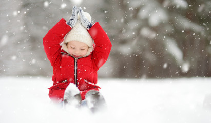 Adorable young girl having fun in beautiful winter park during snowfall. Cute child playing in a snow.