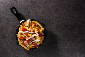 Typical Latin America Salchipapa. Sausages with fries, ketchup, mustard and mayo in iron pan and black background. Top view. Copy space