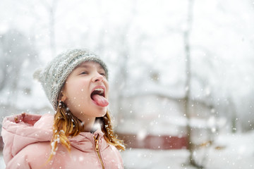 Adorable young girl catching snowflakes with her tongue in beautiful winter park. Cute child...