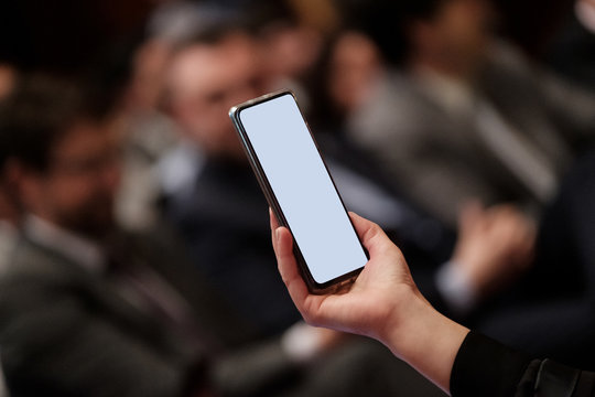 A hand holds a mobile phone in a meeting