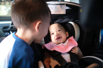 Happy road trip with young kid, Big brother and little sister playing together in car, Cute smiling Asian baby girl child sitting in rear facing car seat.