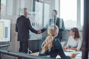 Confident businessmen shaking hands and smiling while working together with colleagues in the board room © gstockstudio