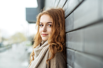 Beautiful adult woman stands near a black wall. Brown knitted sweater and scarf. Fashion concept, lifestyle, urban and autumn.