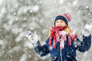 Adorable young girl having fun in beautiful winter park during snowfall. Cute child playing in a snow.