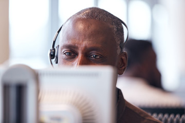 Mature Businessman Wearing Telephone Headset Talking To Caller In Customer Services Department