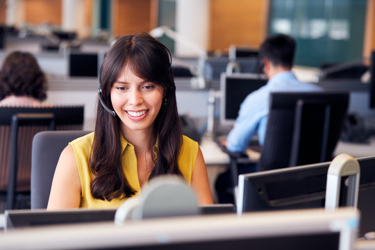 Young Businesswoman Wearing Telephone Headset Talking To Caller In Customer Services Department