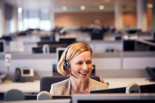 Mature Businesswoman Wearing Telephone Headset Talking To Caller In Customer Services Department