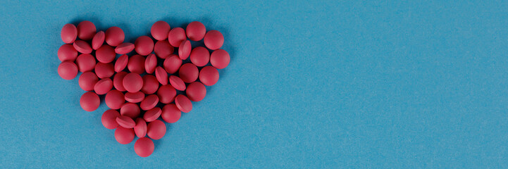 Obraz premium A scattering of red pills in the form of a heart on a blue background. Close-up. Banner.