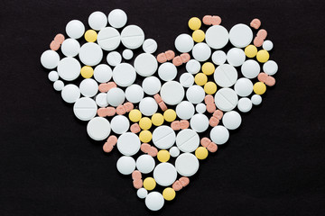 Colorful medical pills on a black background in the shape of a heart, for your text
