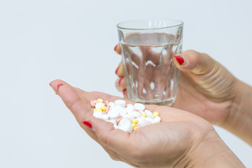 in the girl’s hand a lot of pills and a glass of water on a white background