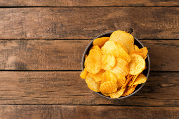 Tasty potato chips in bowl on rustic wooden background with copyspace. Top view