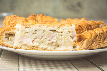 Slices of baked delicious pie with chicken and potatoes in plate on kitchen table.