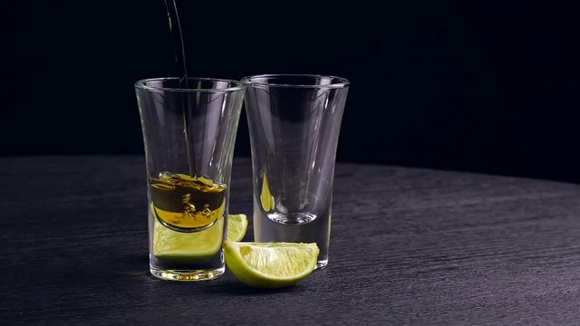 tequila is poured into two glasses on black background
