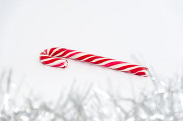 Classic glossy red and white christmas candy cane on white background. Garland in the foreground. Selective focus. Festive Christmas background. Copy space