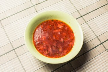 Red soup borsch in green plate on kitchen table.
