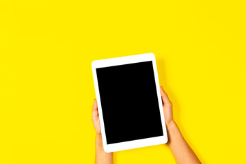 Kid hands holding white tablet computer on yellow background